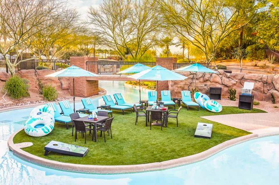 Resort pool area with turquoise umbrellas, lounge chairs, and manicured lawn by water feature