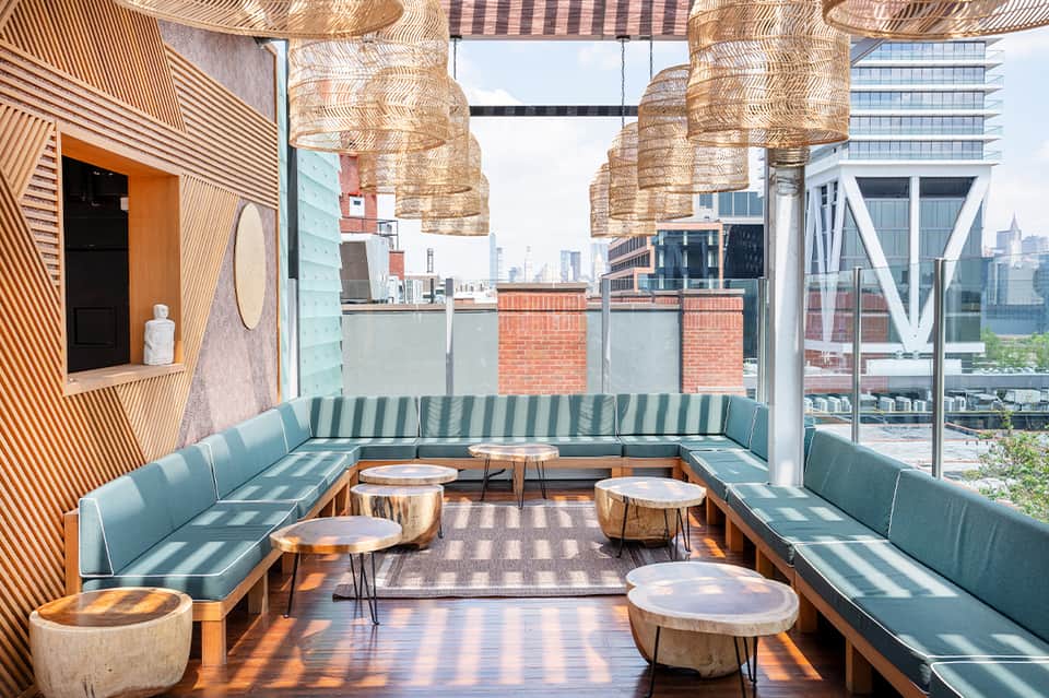 Rooftop lounge with teal seating, woven pendant lights, wood accents overlooking urban skyline