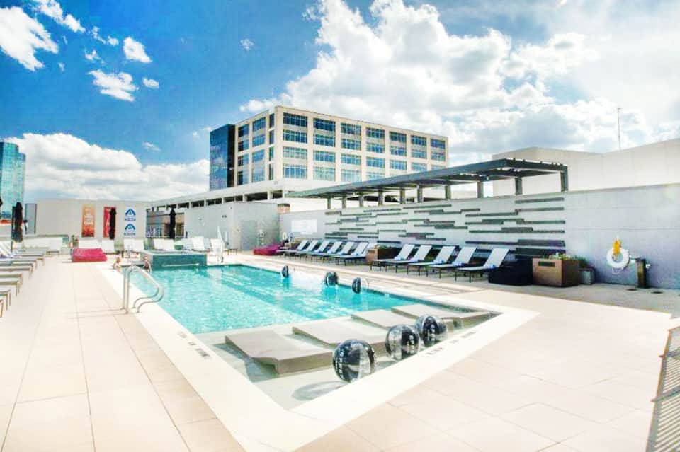 Modern rooftop pool with turquoise water, lounge chairs, white pergola, and multi-story hotel building