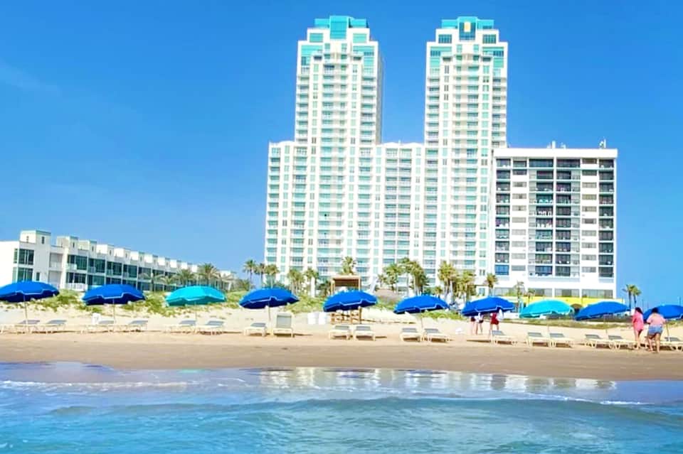 Beachfront resort high-rise towers with blue umbrellas lining sandy beach and turquoise ocean waves
