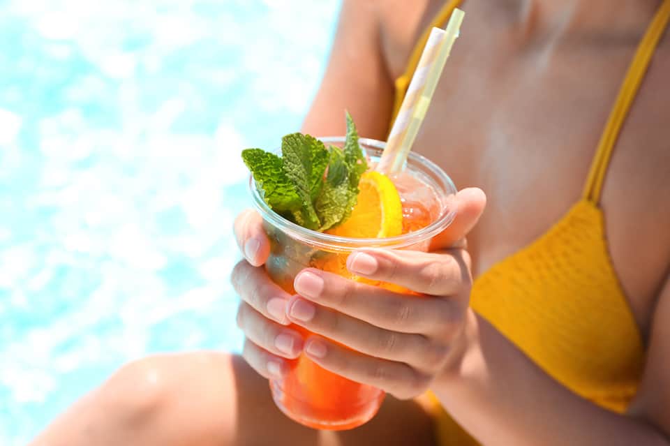 Woman in yellow swimsuit holding coral cocktail with mint garnish by pool