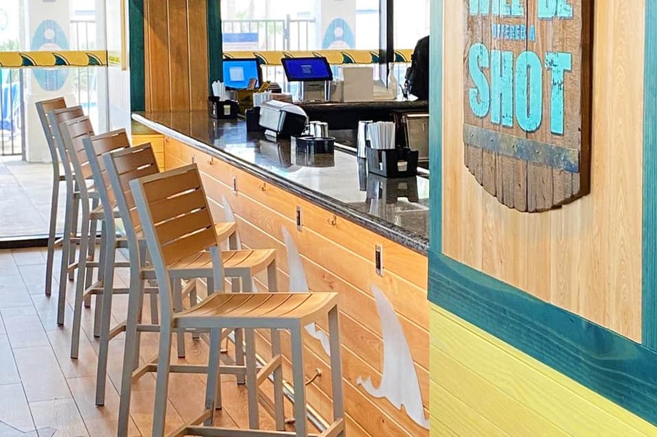 Casual beachside cafe with bar seating, ocean view, and turquoise signage