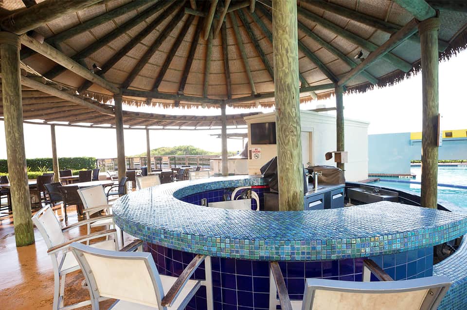 Circular tiki bar with blue tile counter overlooking resort pool and ocean