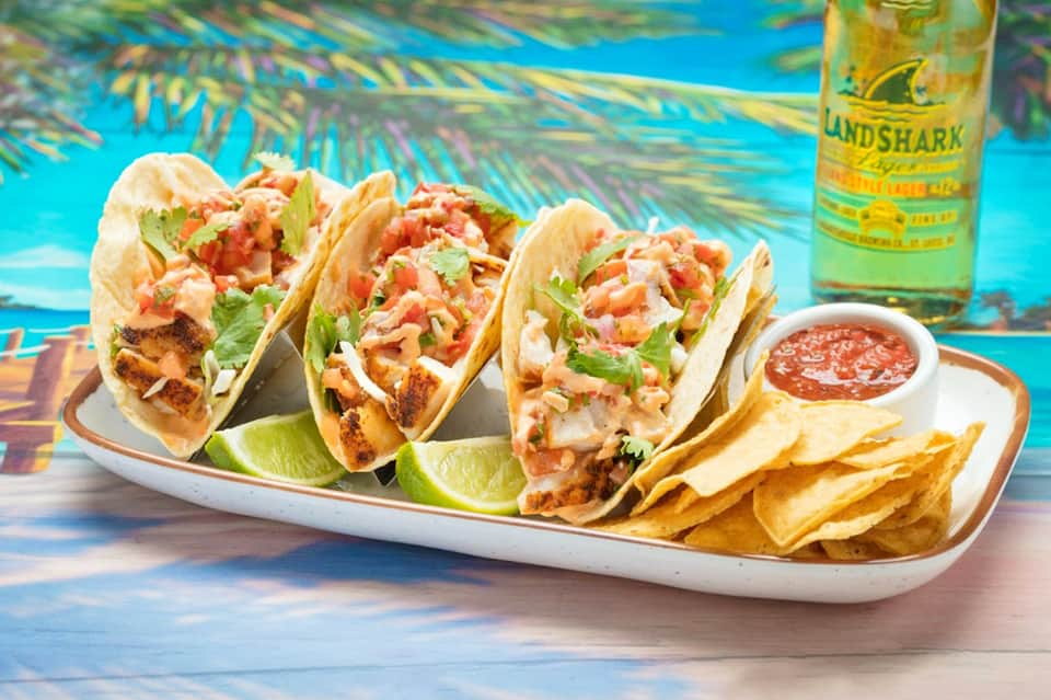 Three fish tacos with cilantro and lime on white plate with chips and salsa