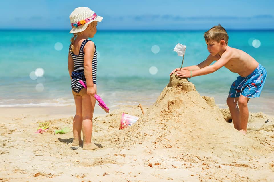Children building sandcastle on beach with clear turquoise ocean and white sand