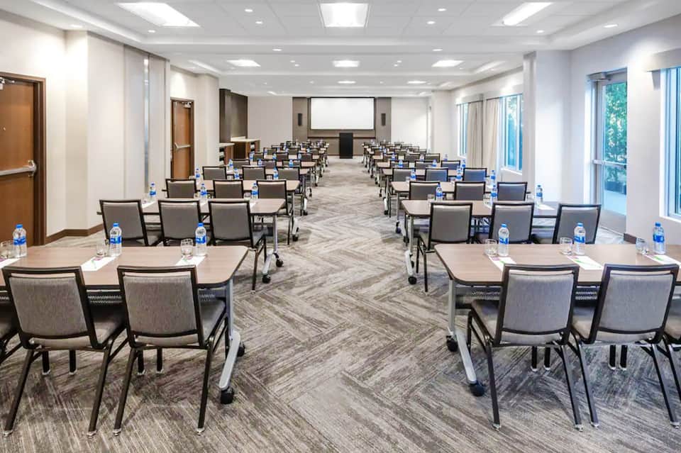Conference room with classroom-style seating, projection screen, and large windows with natural light