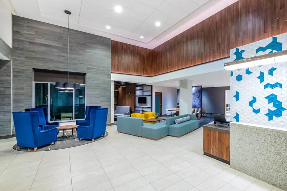 Contemporary hotel lobby featuring blue and turquoise seating, geometric wall art, and mixed material finishes
