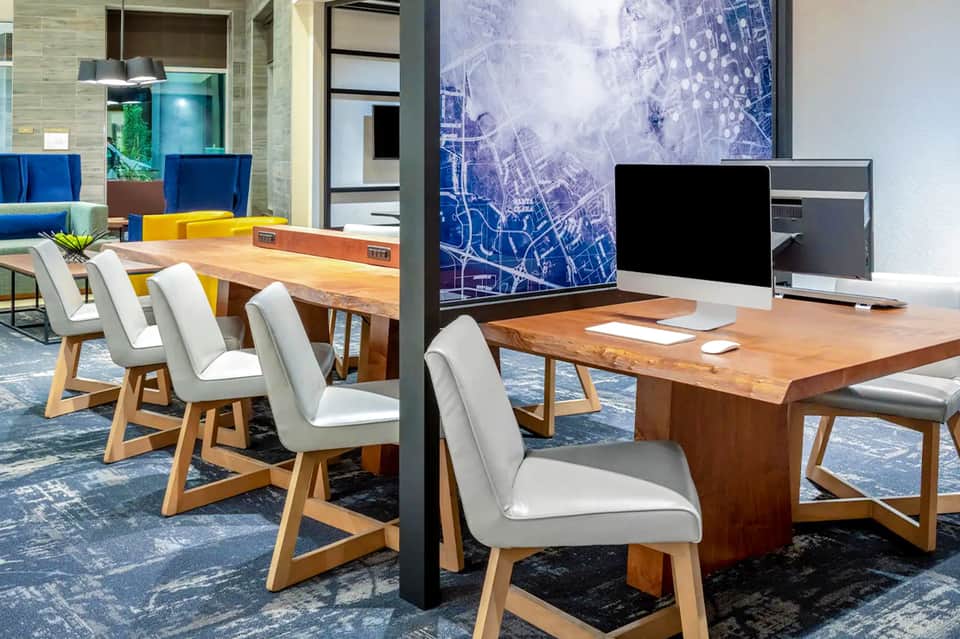Modern office workspace with wooden desks, white chairs, computer monitors, and blue accent wall art