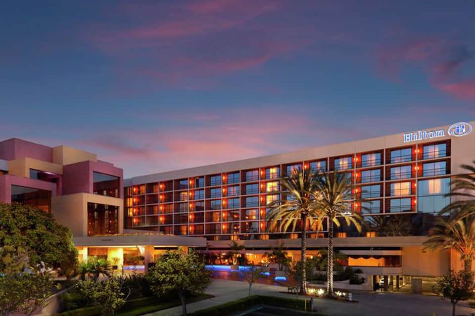 Modern Hilton hotel exterior at dusk with illuminated rooms and palm trees