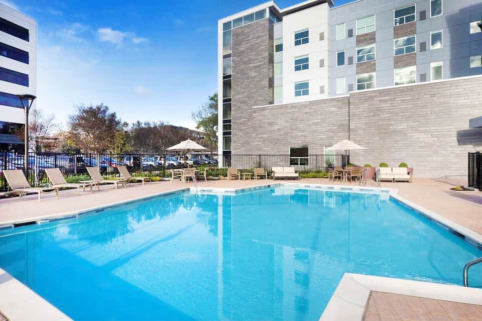 Resort outdoor pool with modern building, lounge chairs, and umbrellas