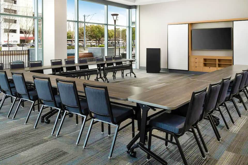 Modern conference room with long dark table, blue chairs, large windows overlooking outdoor area