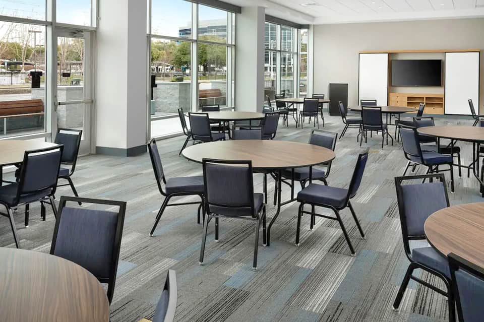 Contemporary hotel gathering space with round tables, comfortable seating, and large windows