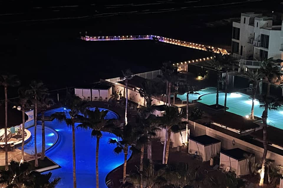 Nighttime aerial view of illuminated resort pools and grounds by the ocean