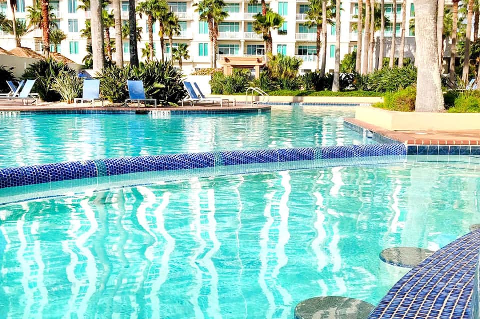 Lap pool with lane dividers at resort, flanked by palm trees and multi-story hotel building