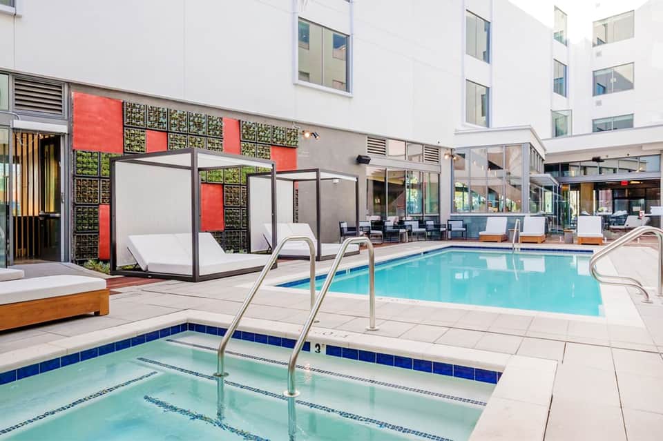 Indoor resort pool with colorful modular cabanas, modern lounge seating, and multi-story white building backdrop