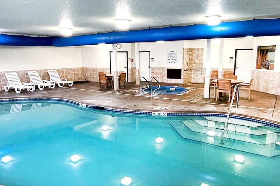 Indoor heated pool facility with white lounge chairs and blue ceiling pipes