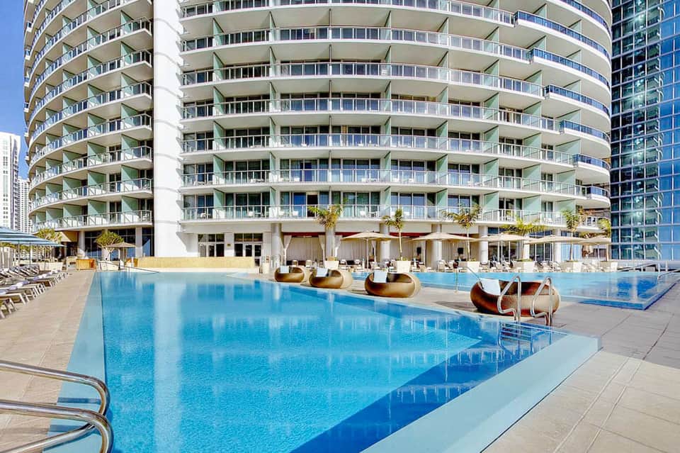 Curved high-rise residential tower with large outdoor swimming pool and lounge seating area