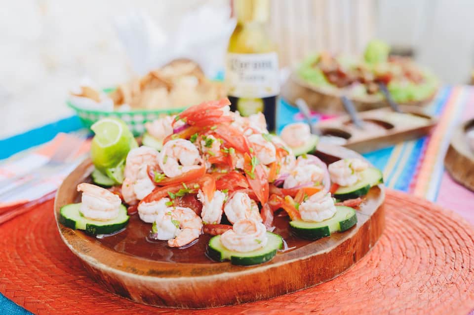 Plate of fresh shrimp ceviche appetizers on cucumber slices with red pepper garnish and colorful striped table linens