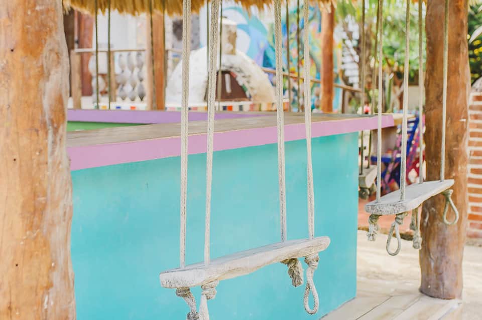 Wooden swings with rope on a covered patio overlooking turquoise water