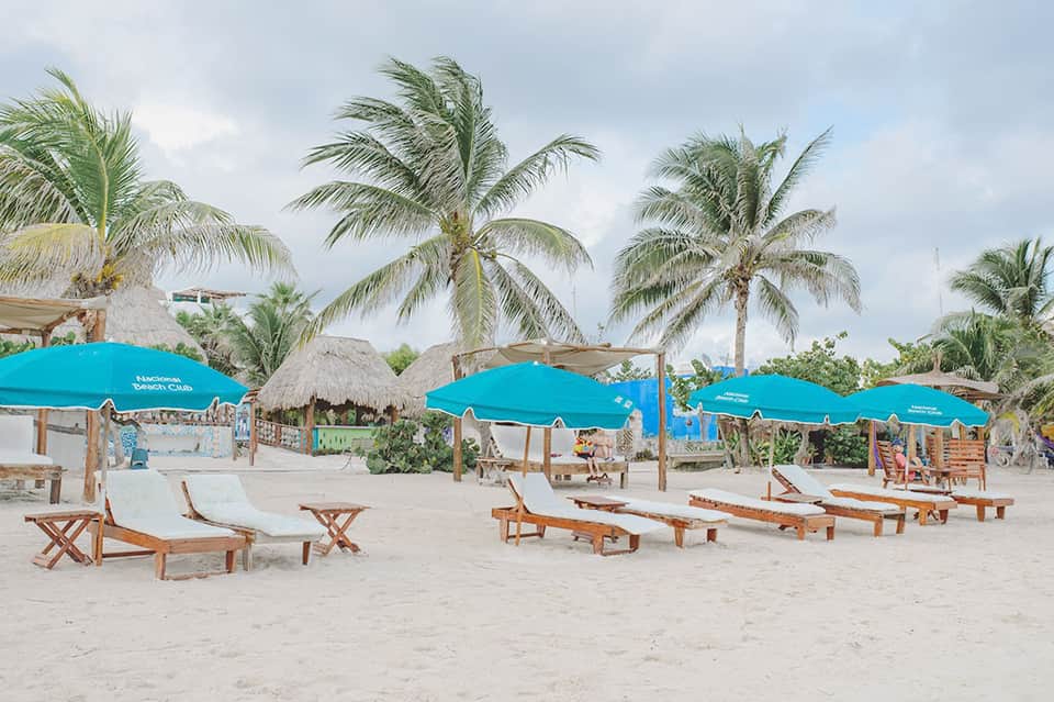 Sandy beach with turquoise umbrellas, lounge chairs, and palm trees