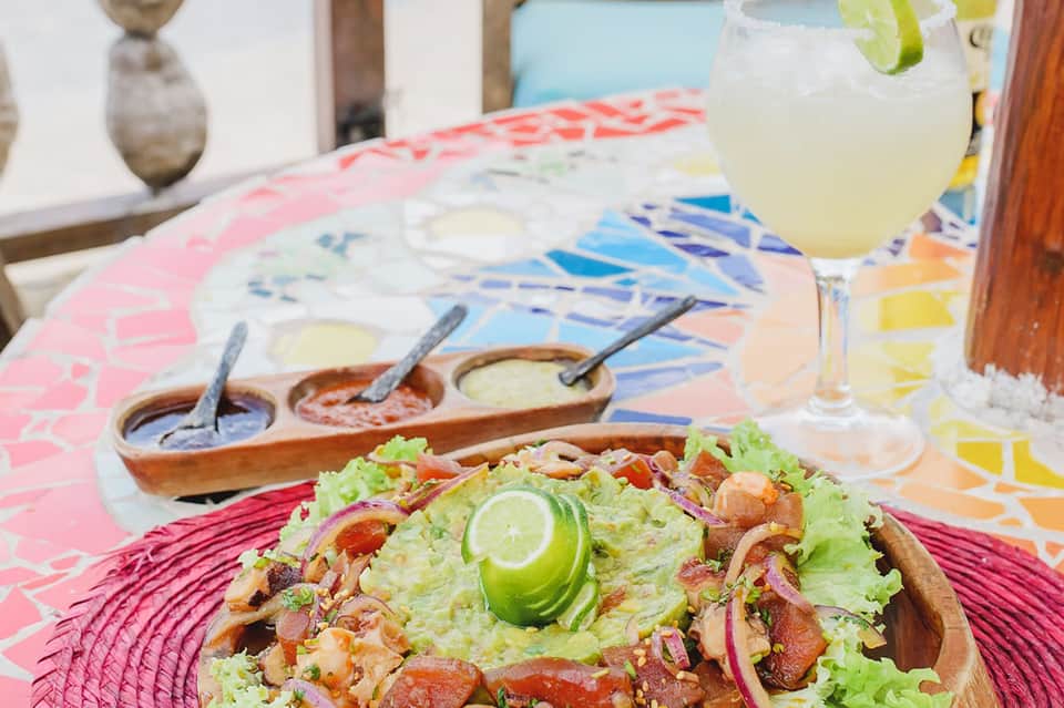 Beachfront dining plate with fresh seafood taco, fresh lime, and colorful patterned table with cocktail