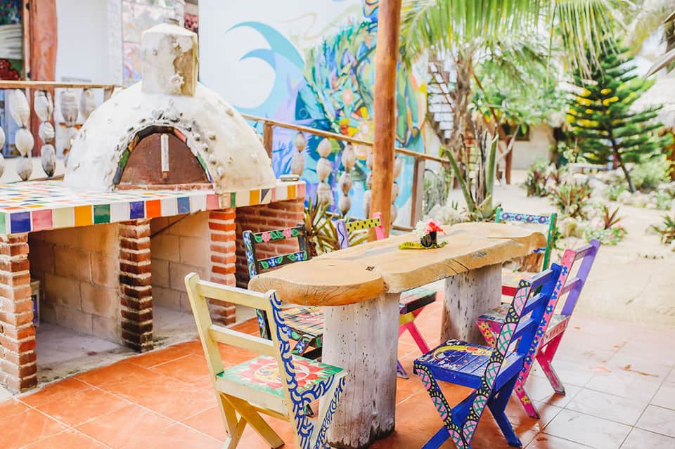 Colorful outdoor dining area with pizza oven, painted chairs, and tropical plants
