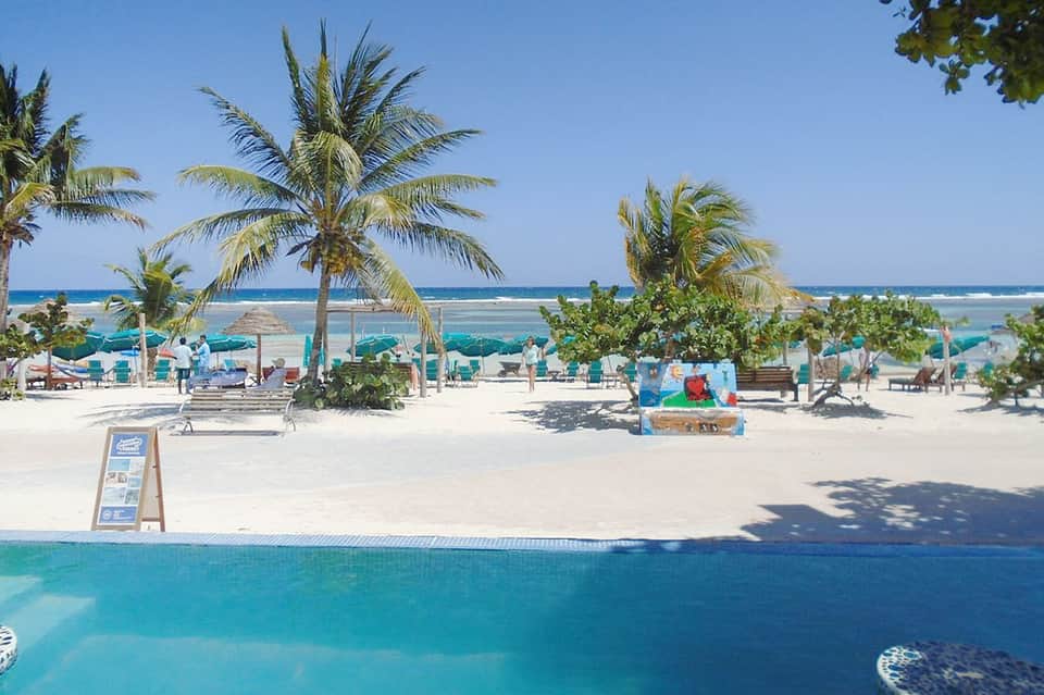 Tropical beach with palm trees, umbrellas, lounge chairs, and clear turquoise ocean water