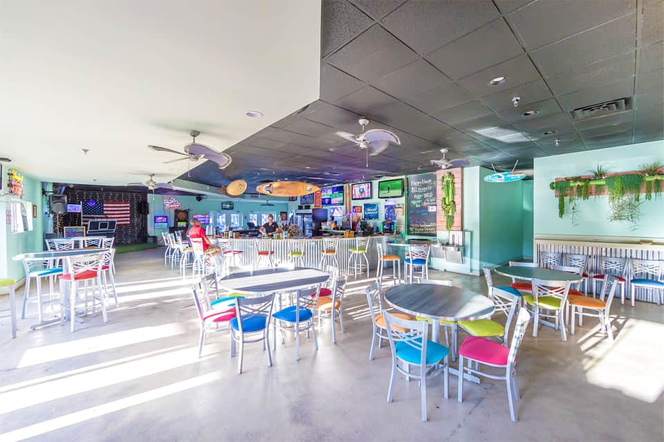 Casual beachside restaurant interior with colorful chairs, bright turquoise walls, and tropical decor
