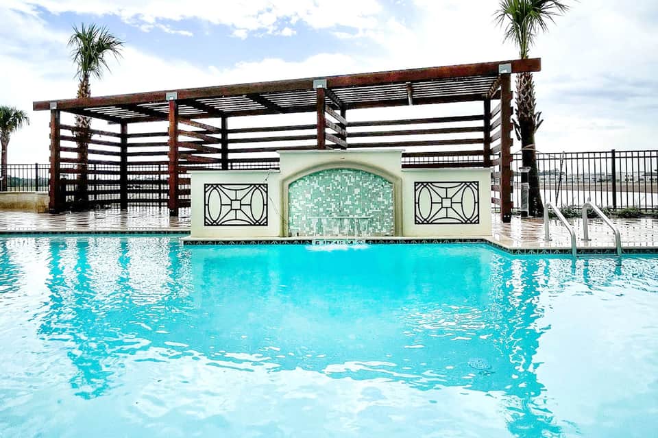 Spa pool with wooden pergola structure and decorative mosaic wall feature in modern resort setting