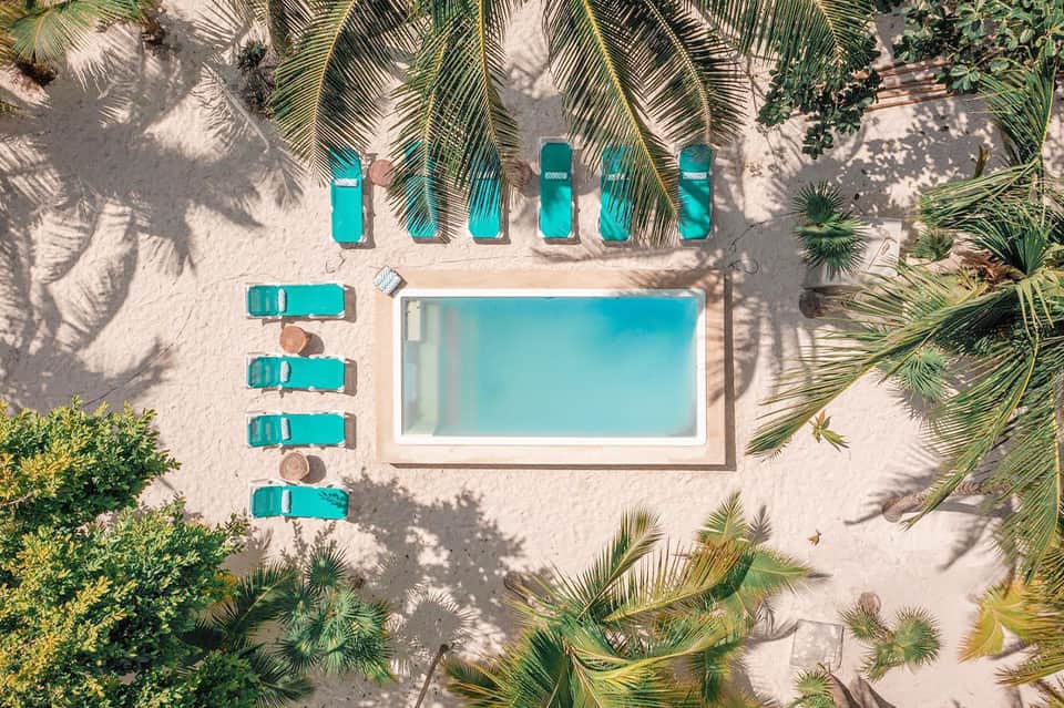 Aerial view of resort pool surrounded by turquoise lounge chairs, palm trees, and sand beach