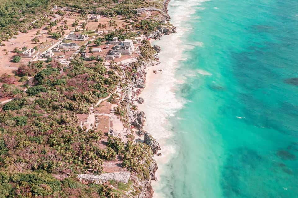 Aerial view of beachfront resort nestled on cliff with turquoise ocean water and dense tropical forest