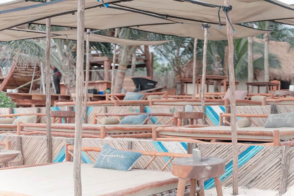 Beach cabana with wooden posts, shade canopy, striped cushions, and palm trees at sunset