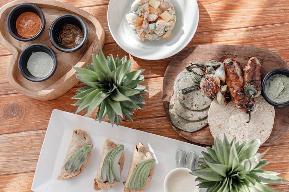 Overhead view of grilled meats, tacos, seafood ceviche, and various sauces on wooden table