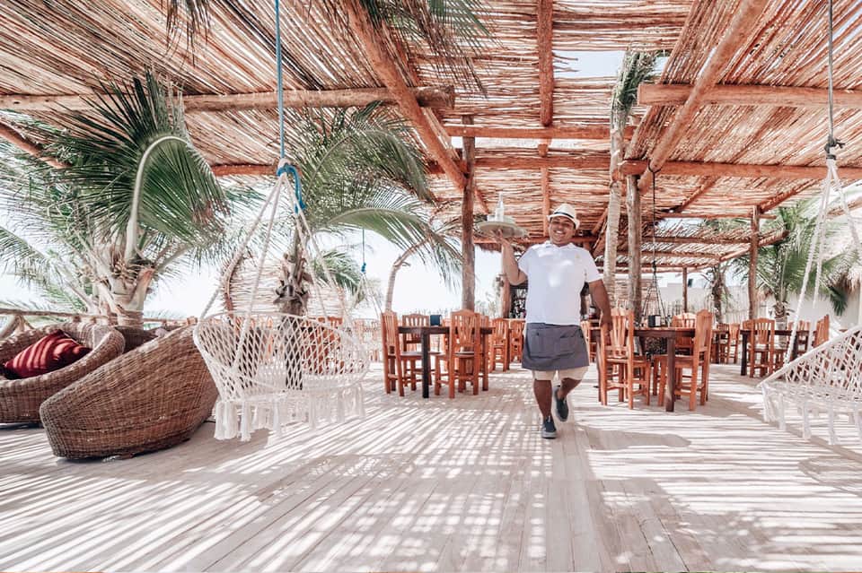 Beachfront wooden pavilion with woven chairs, palm trees, and rustic island decor