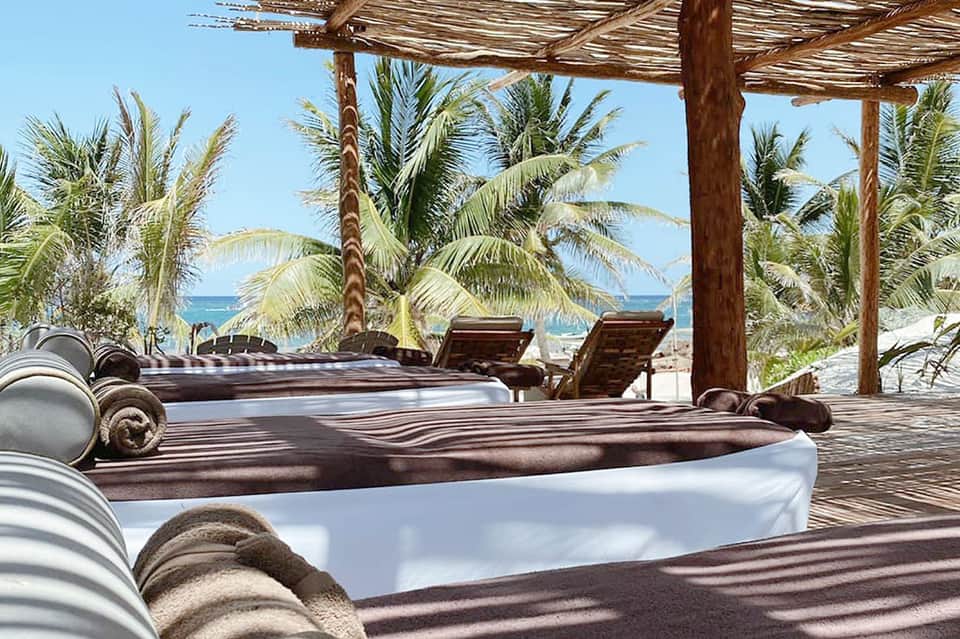 Beach club with lounge beds under wooden pergola overlooking ocean and palm trees