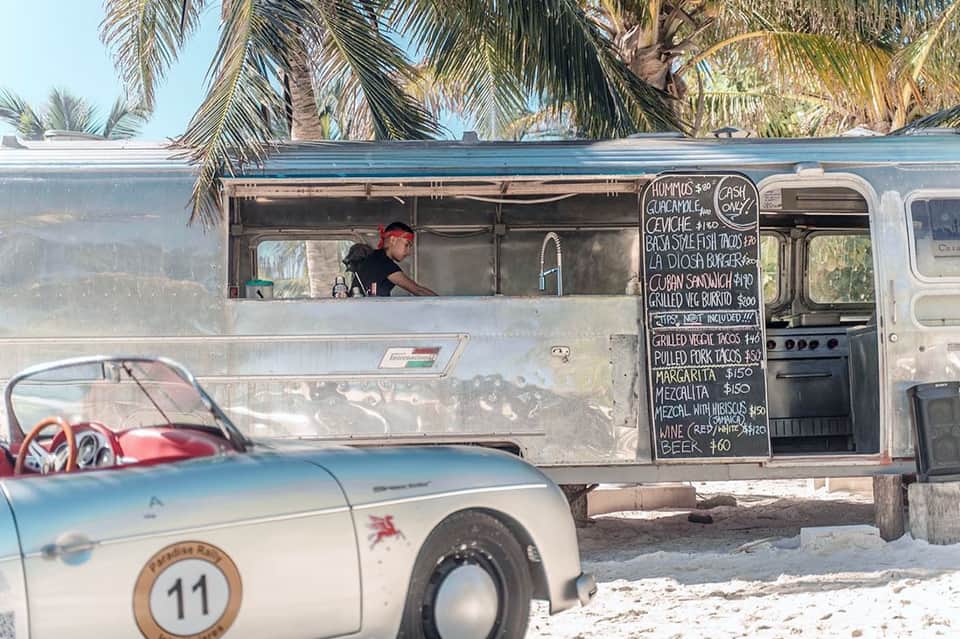 Food truck on a beach with vintage convertible car, palm trees, and ocean backdrop