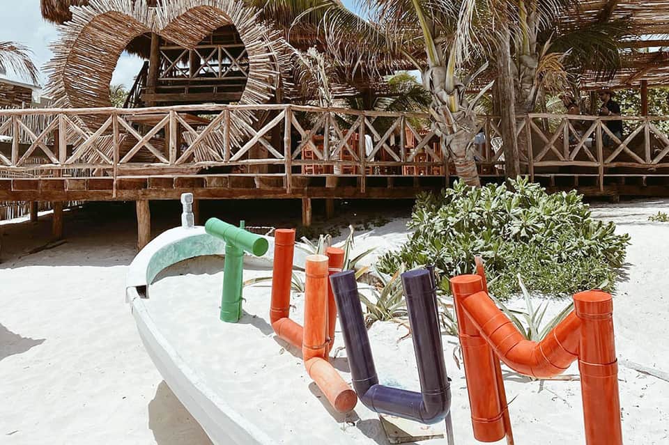 Beachfront wooden deck with colorful play equipment and palm-thatched structures on white sand