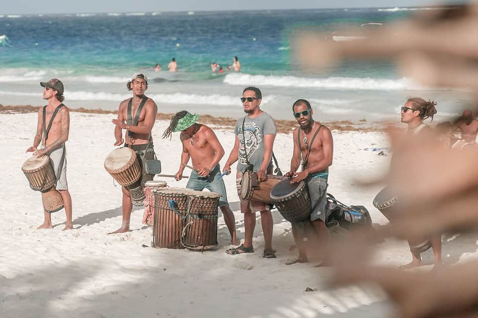 Beach musicians performing with drums in sand with ocean and swimmers