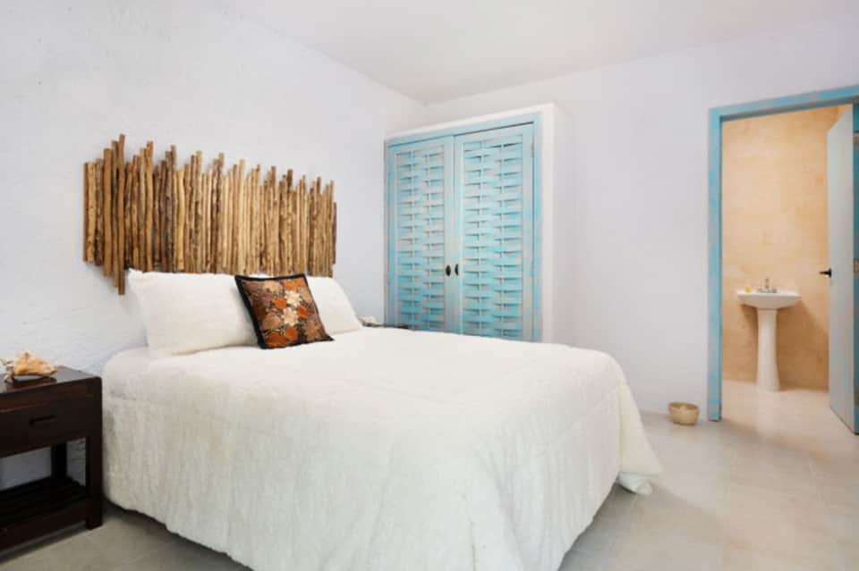 Coastal bedroom with white bed, blue shutters, and wooden headboard accent.