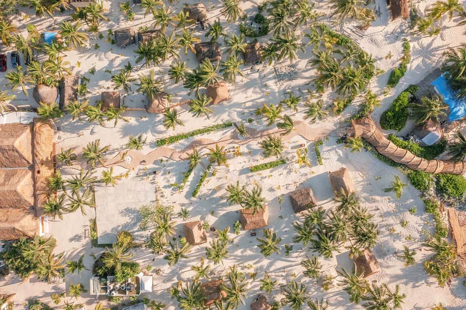 Aerial view of beachfront resort with palm trees, buildings, and swimming pools on sand