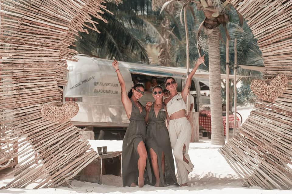 Three women posing at beach gate structure with palm trees and tropical vacation setting