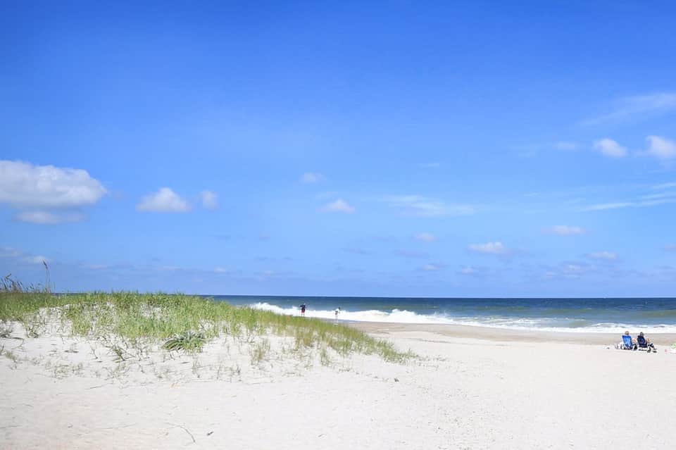 Sandy beach with dune grass, gentle waves, and clear blue sky on a sunny day
