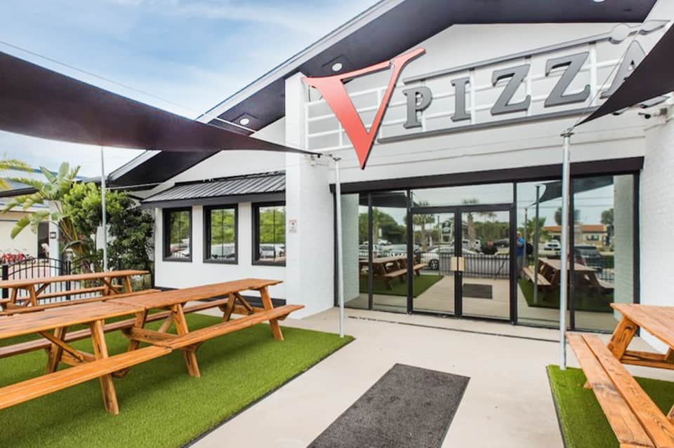 Contemporary pizza restaurant exterior with wooden picnic tables on artificial grass patio