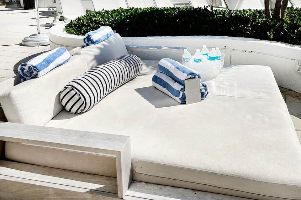 Luxury hot tub with rolled towels, striped pillows, and water bottles on a white deck