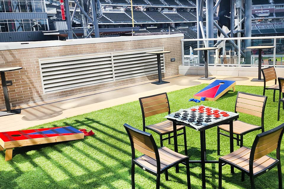 Outdoor recreation area with cornhole, checkers game, and grass overlooking stadium