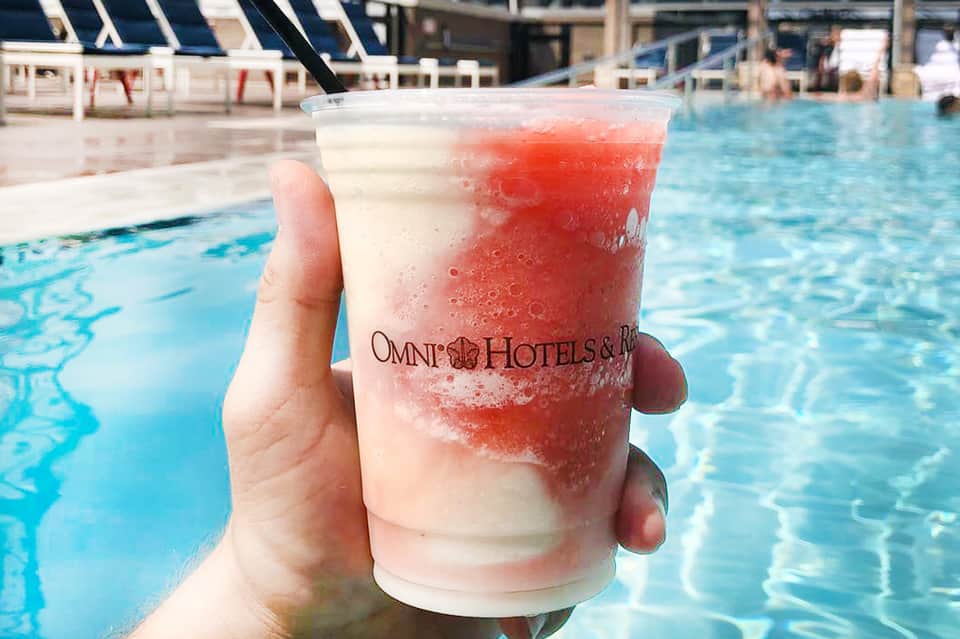 Red cocktail drink with Omni Hotels logo held poolside with lounge chairs