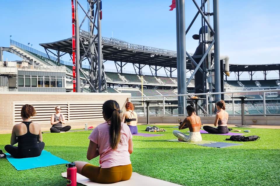 Group yoga class on grass field inside sports stadium with instructor leading session