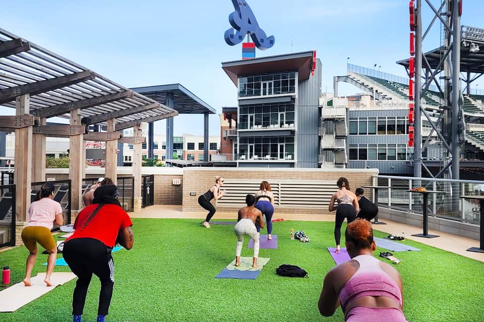 Group fitness class on artificial grass rooftop with city buildings and sports structures visible in background