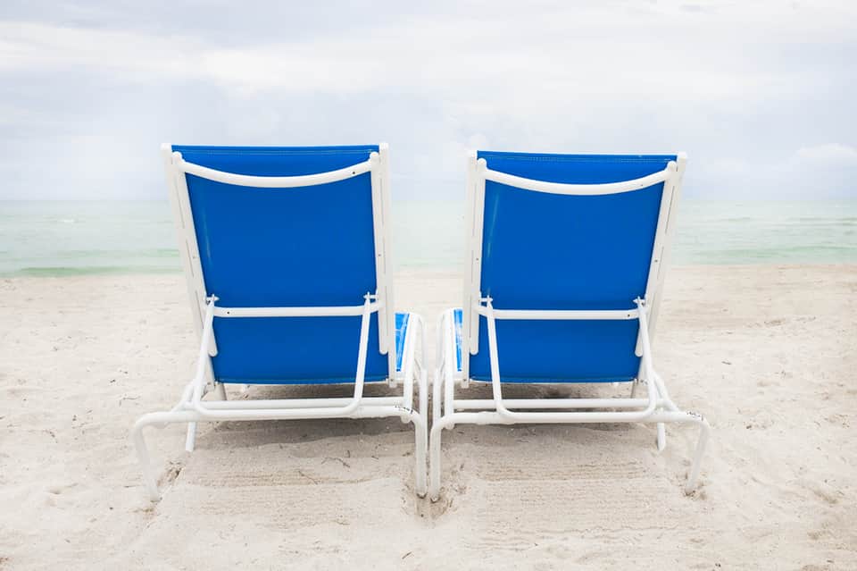 Two blue and white beach chairs facing the ocean on sandy shore with calm waves