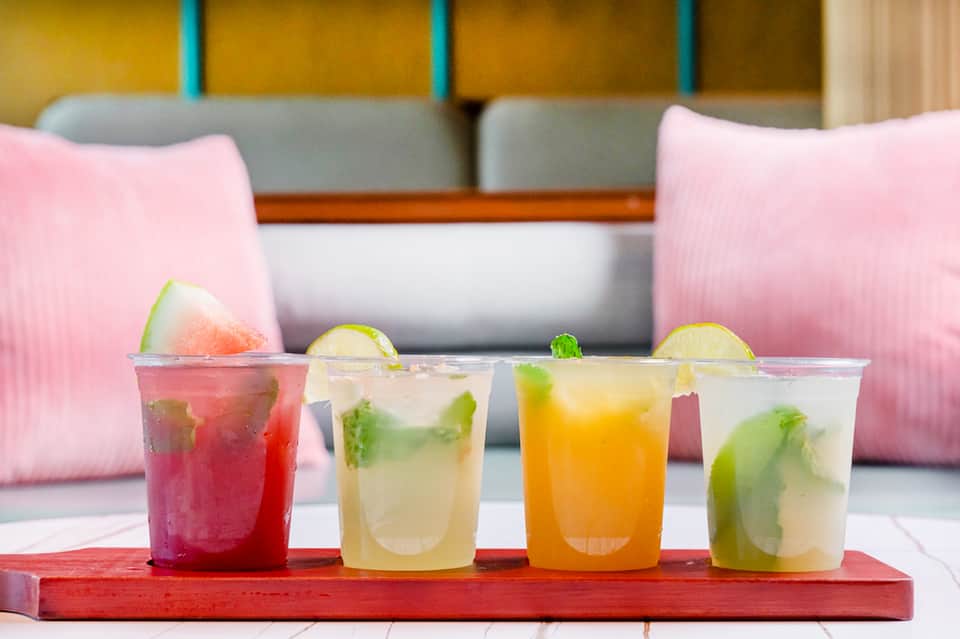 Four colorful craft cocktails with fruit garnishes displayed on a red tray